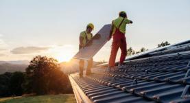 Image where two men are installing solar panels on a roof during sunset.