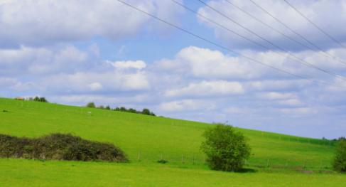 UK electricity pylon in a green field with bright blue sky